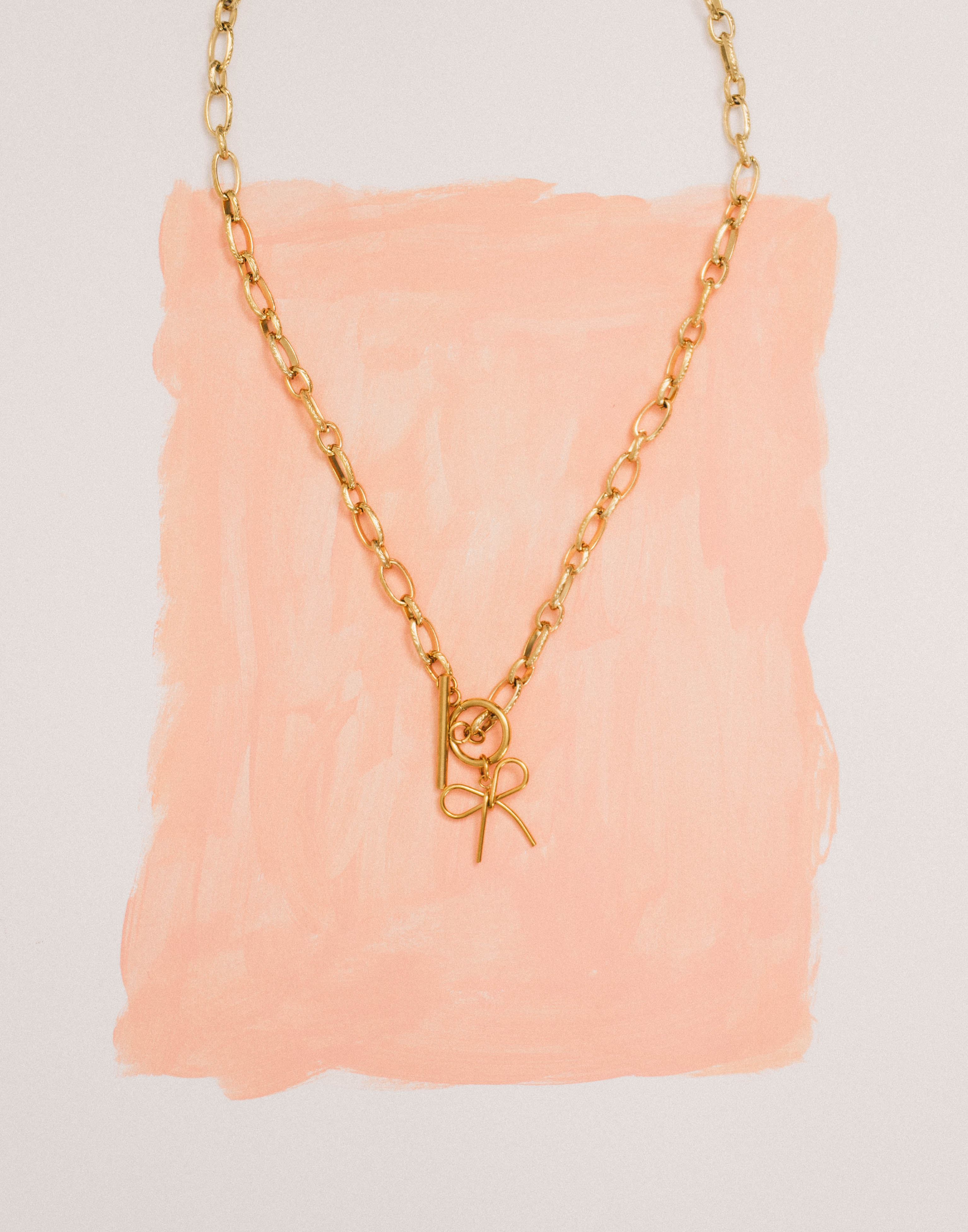Gold necklace with a bow charm on a pink textured background