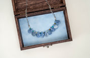 blue gemstone necklace resting in a wooden box lined with blue velvet