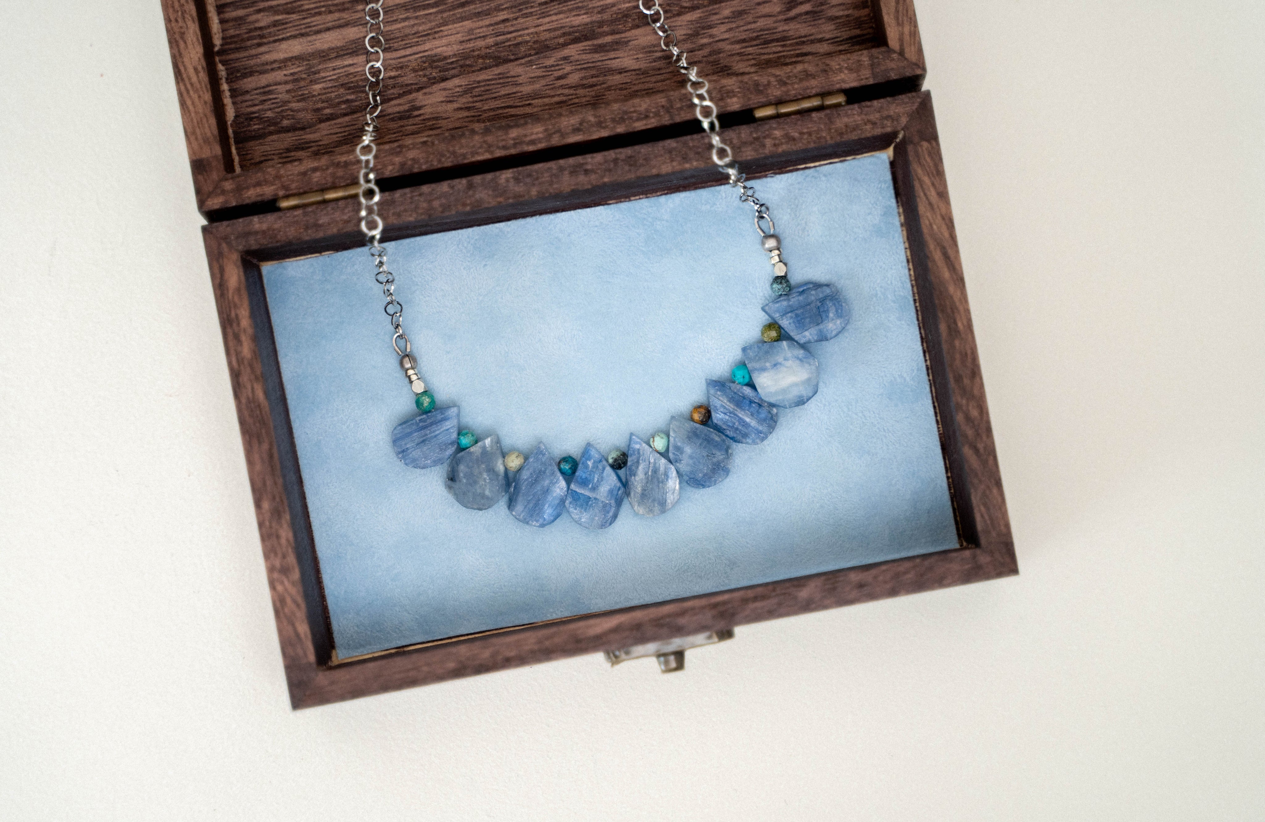 blue gemstone necklace resting in a wooden box lined with blue velvet