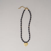 Necklace with black beads and a gold heart-shaped pendant on a gray background