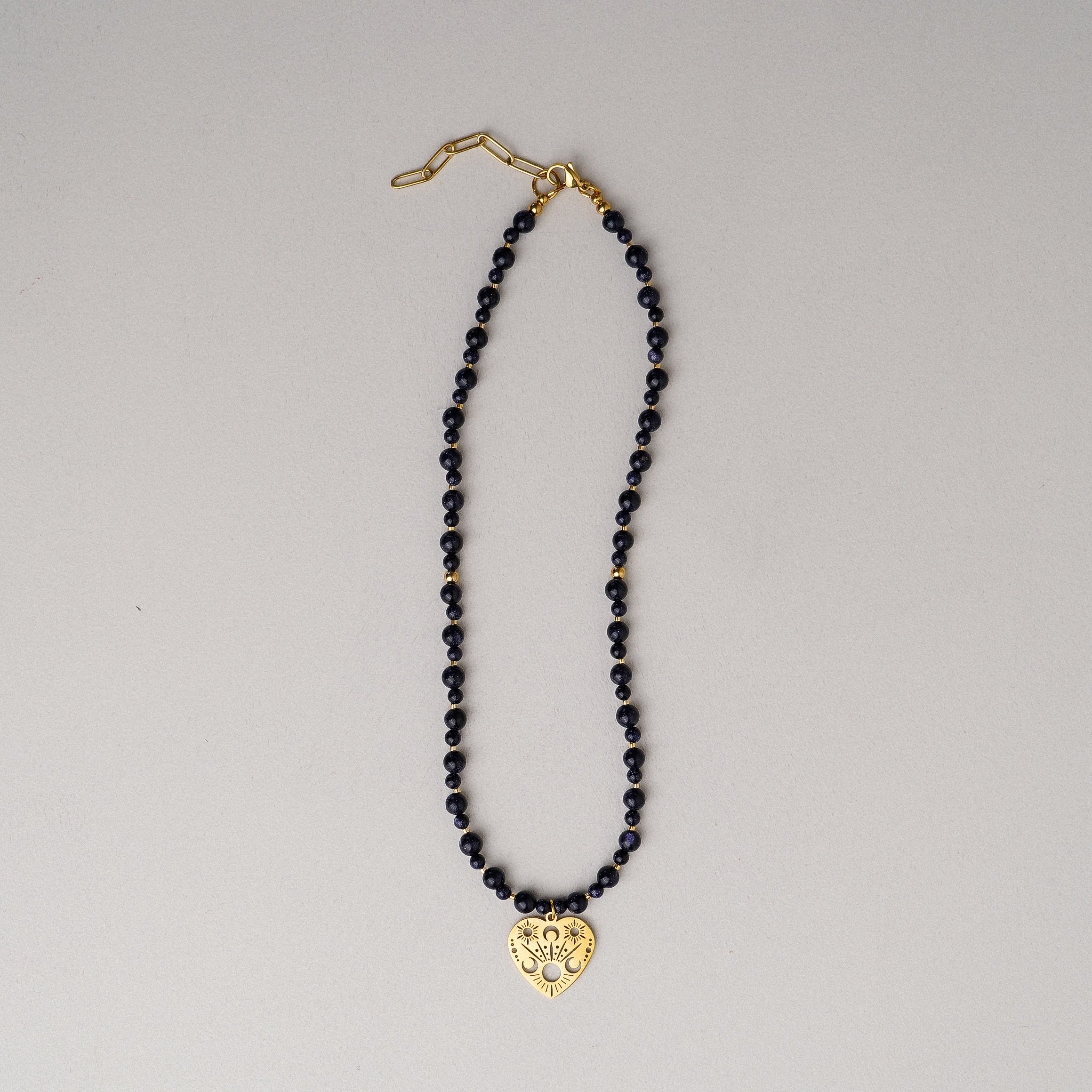 Necklace with black beads and a gold heart-shaped pendant on a gray background