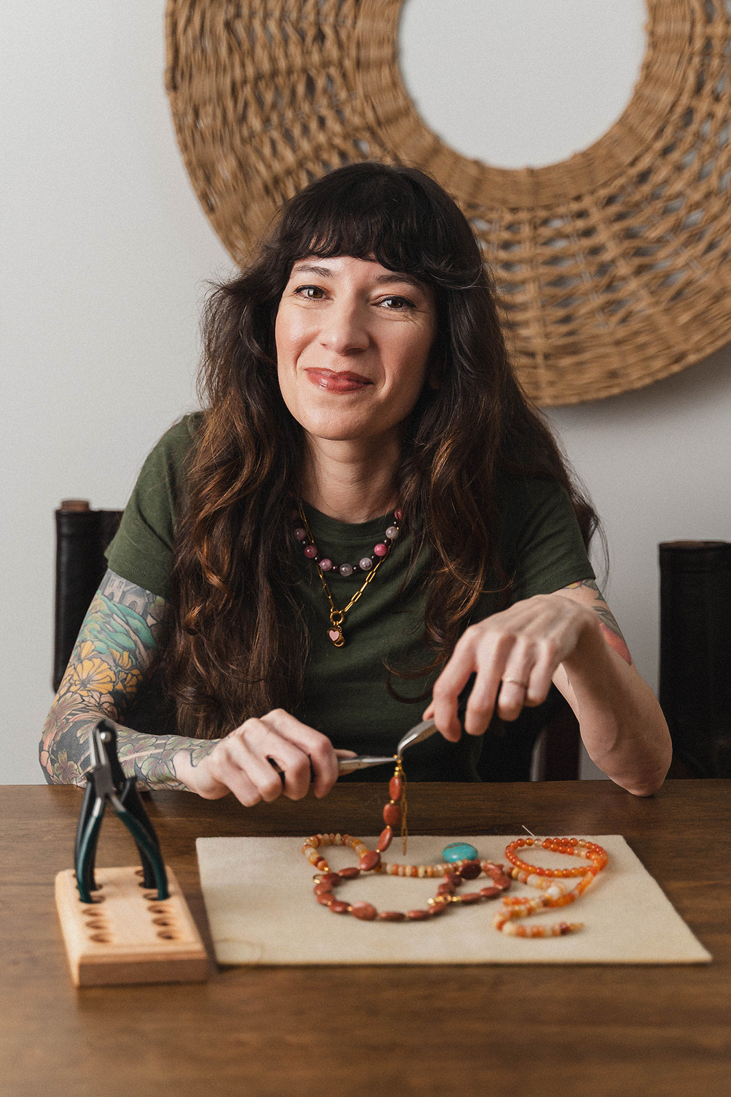 Woman sitting at a table making jewelry with beads and tools.