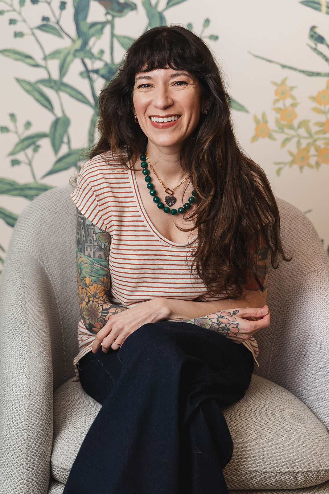 Woman sitting on a couch with floral wallpaper in the background