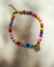A beaded necklace with multicolored round beads and a gold butterfly charm, displayed on a light beige background with soft shadows.