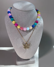 A two-layer necklace displayed on a gray fabric jewelry bust. The top layer features a strand of colorful round beads in pink, blue, yellow, green, and white.