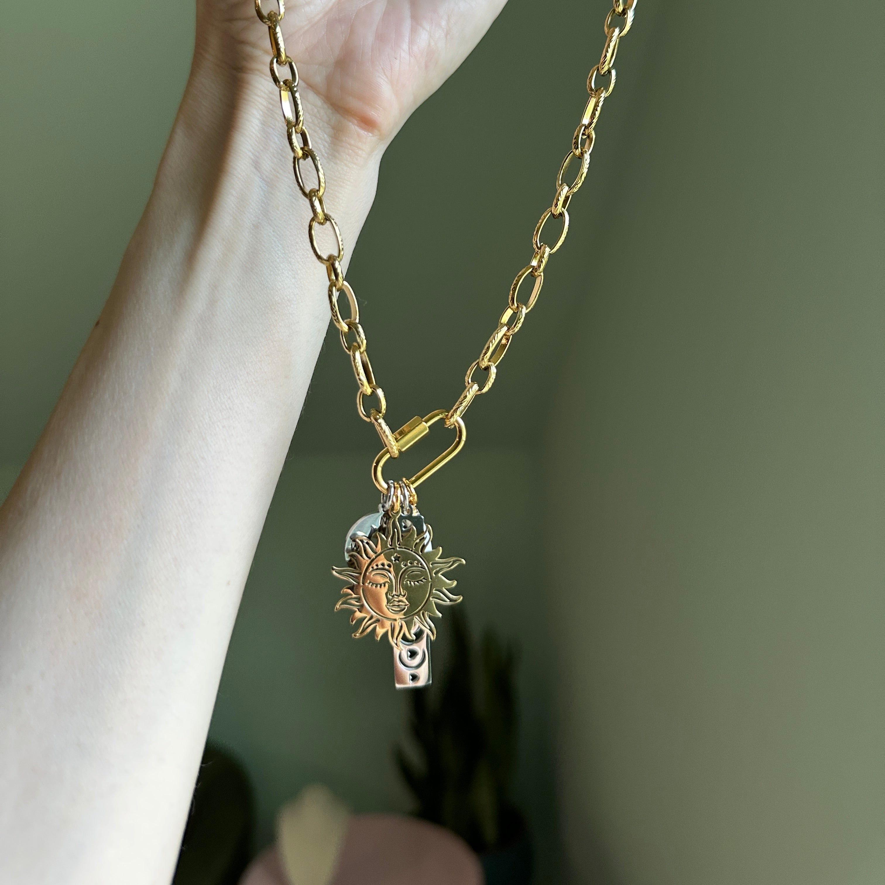 Gold chain with a sunflower pendant held by a hand against a neutral background