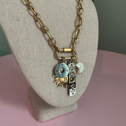 Gold bracelet with charms on a mannequin arm against a pink background