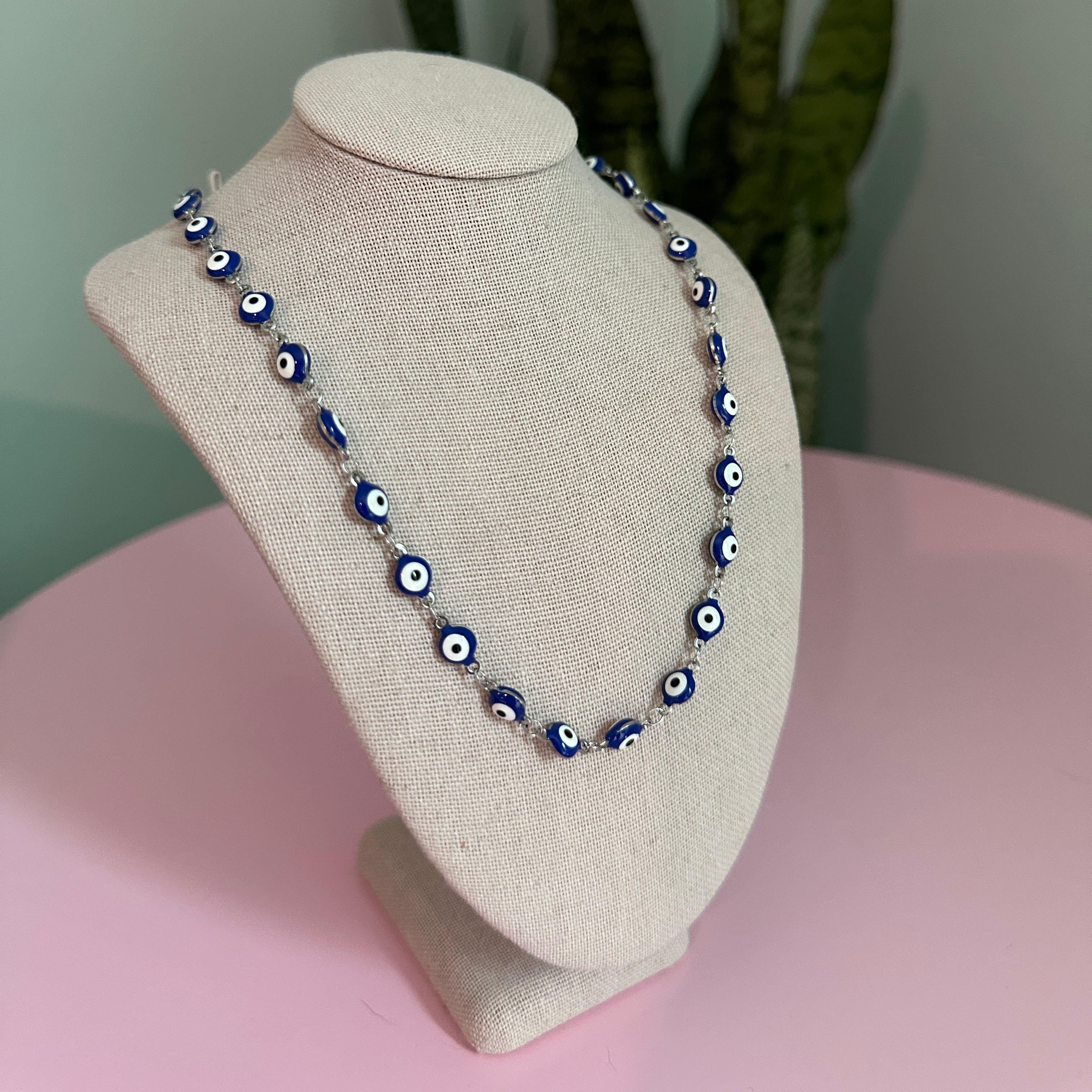 Necklace with blue and white beads on a beige display stand against a pink and green background