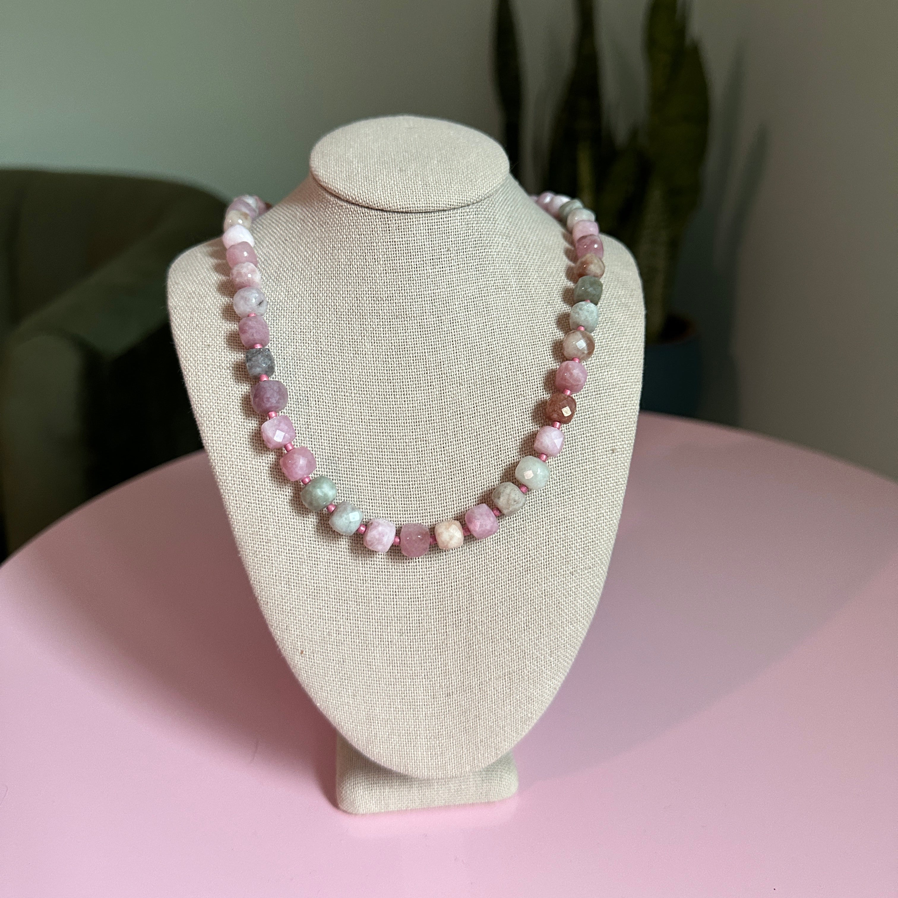 Beaded bracelet on a beige display stand with a pink background