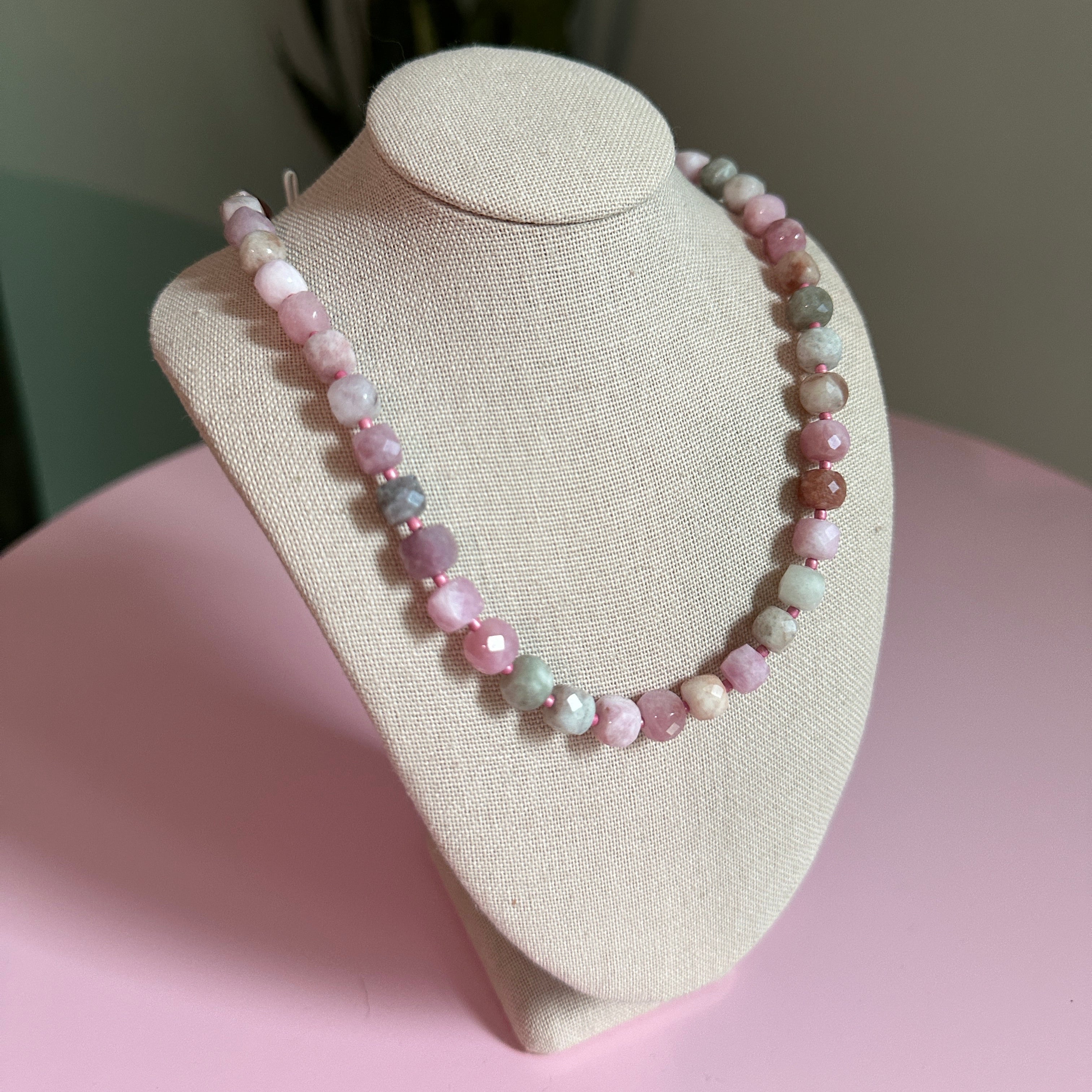 Beaded bracelet on a beige display stand against a pink background