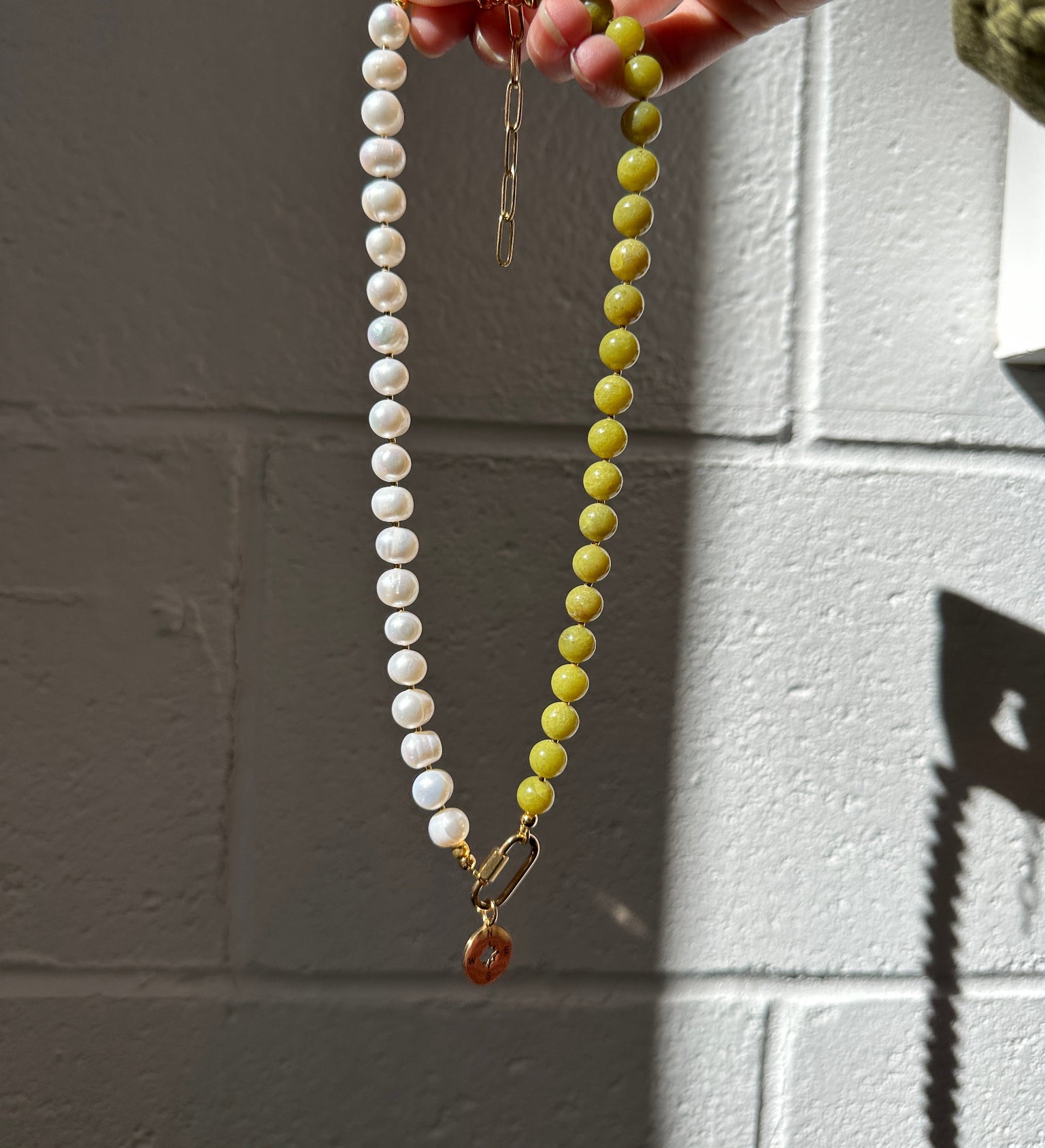 Necklace with green and white beads held by a hand against a tiled wall.