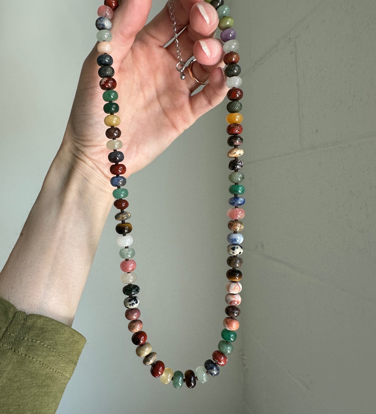 Hand holding a multicolored beaded necklace against a plain background