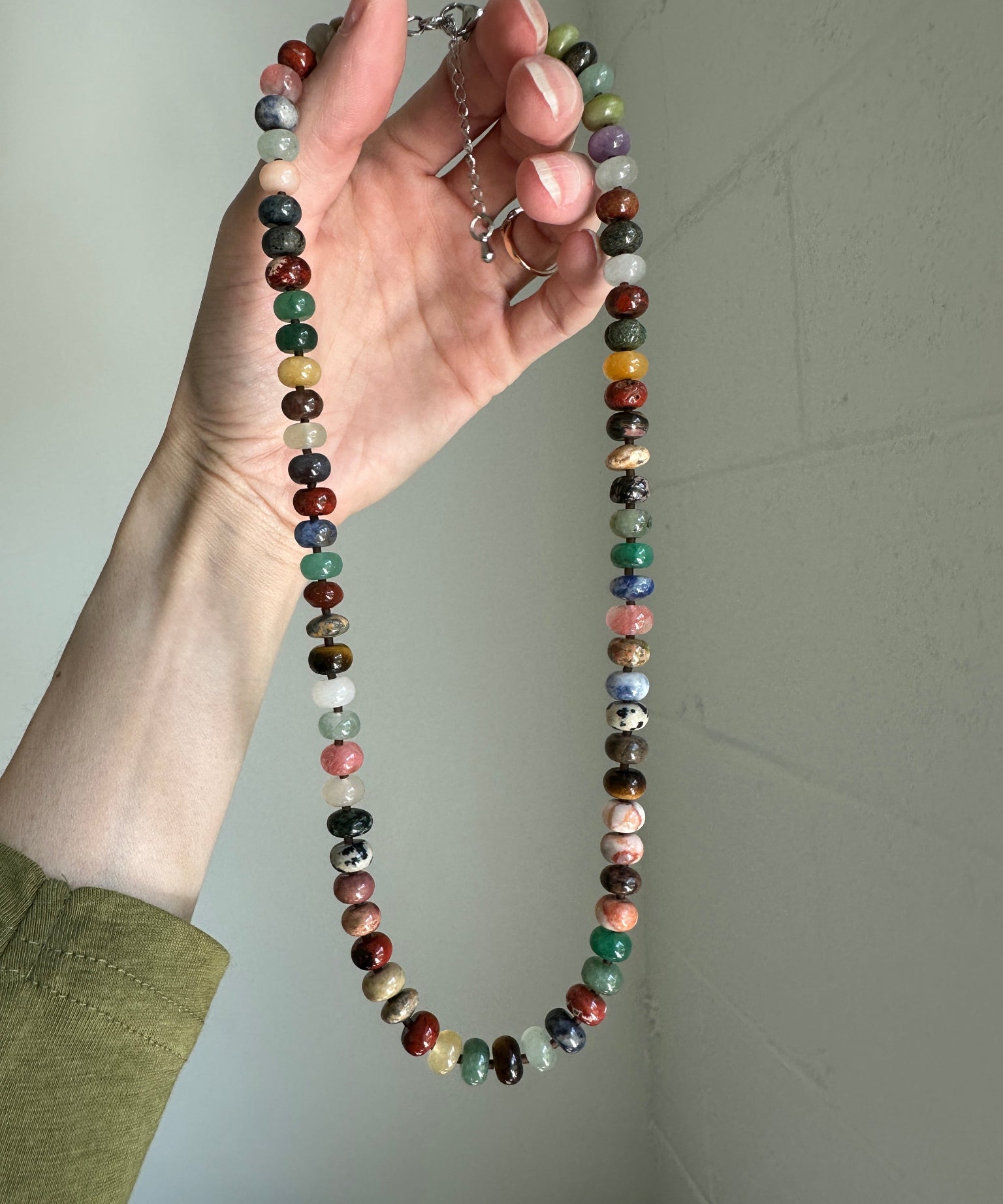 Hand holding a multicolored beaded necklace against a plain background