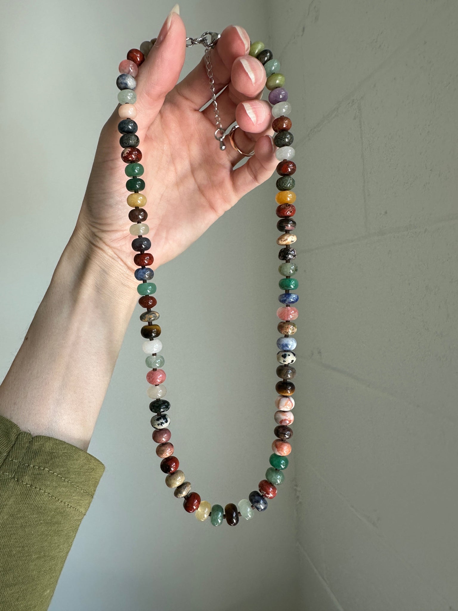 Hand holding a multicolored beaded necklace against a plain background