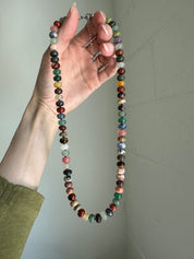 Hand holding a multicolored beaded necklace against a plain background