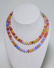 A double-strand beaded necklace displayed on a white fabric-covered jewelry bust. The necklace features small, polished, oval-shaped beads in a variety of bright colors including orange, yellow, green, purple, pink, and blue.