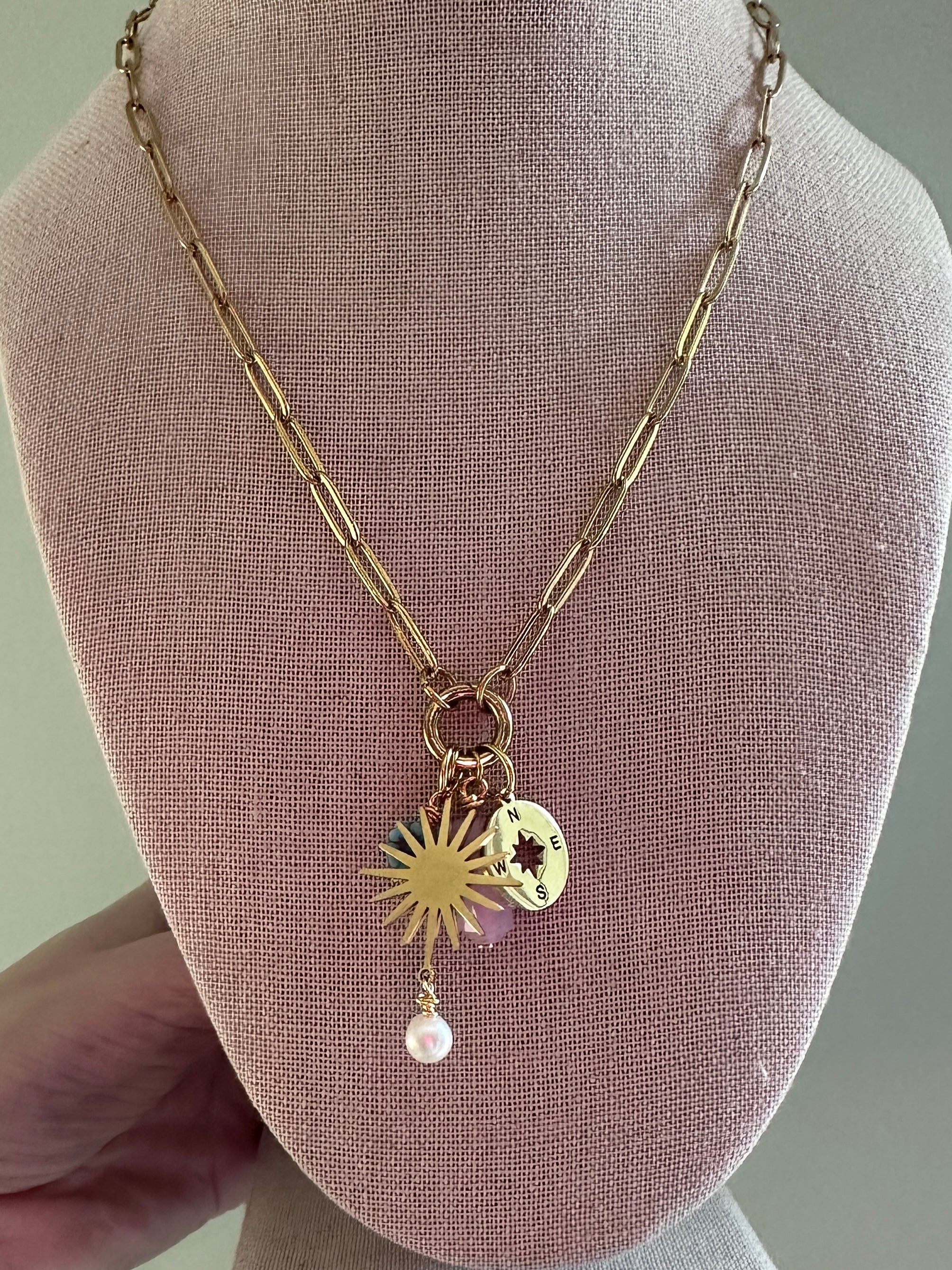 Gold necklace with sun pendant and pearl on a mannequin bust.