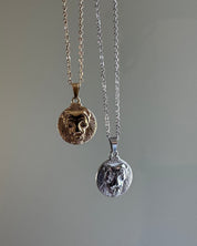 Two lion head pendants on chains against a gray background