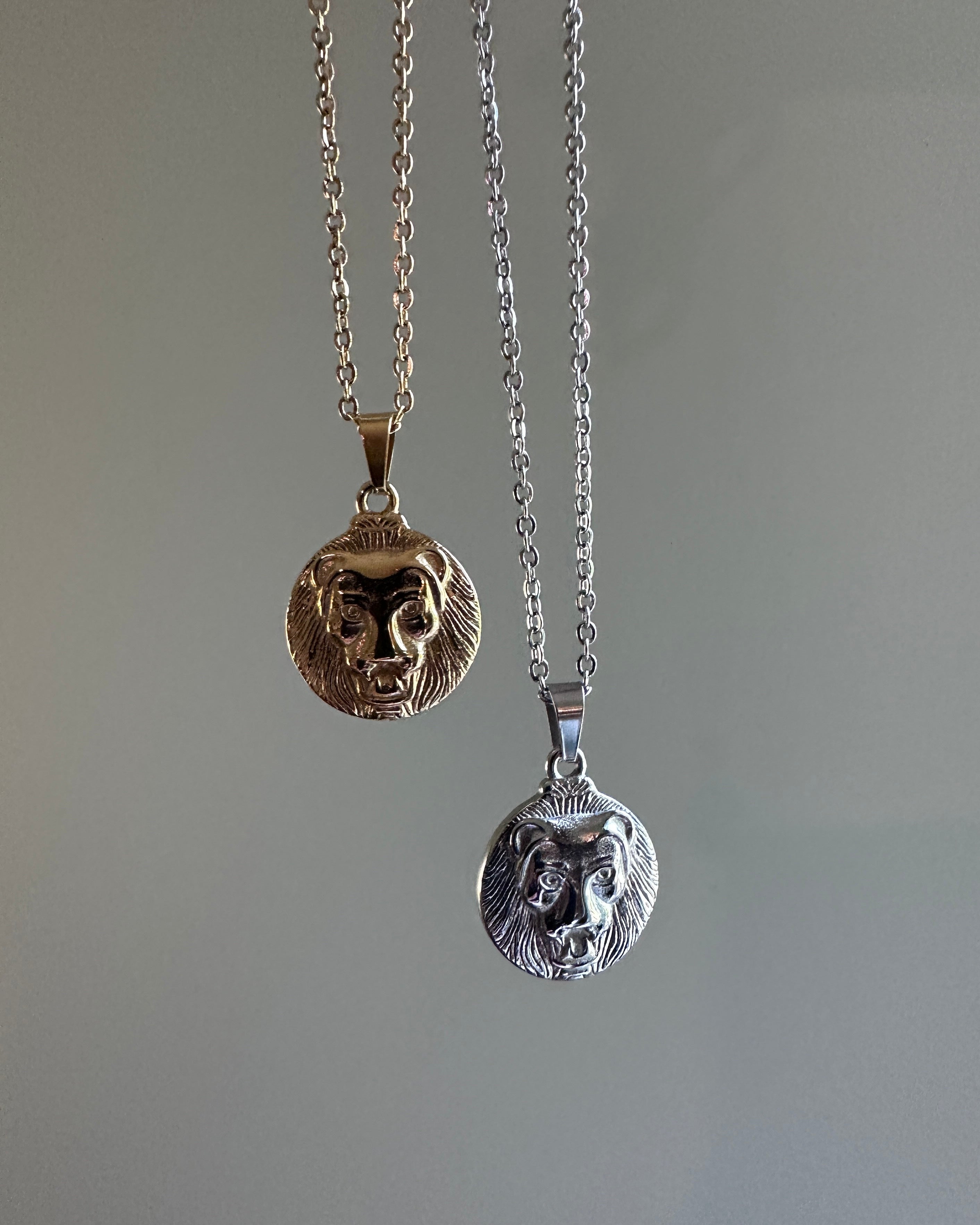 Two lion head pendants on chains against a gray background