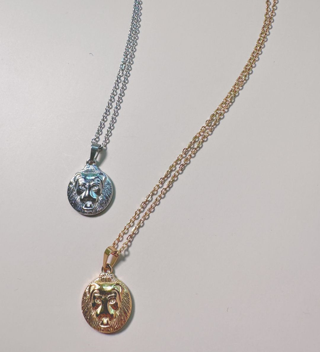 flat lay of two lion charm necklaces in gold and silver