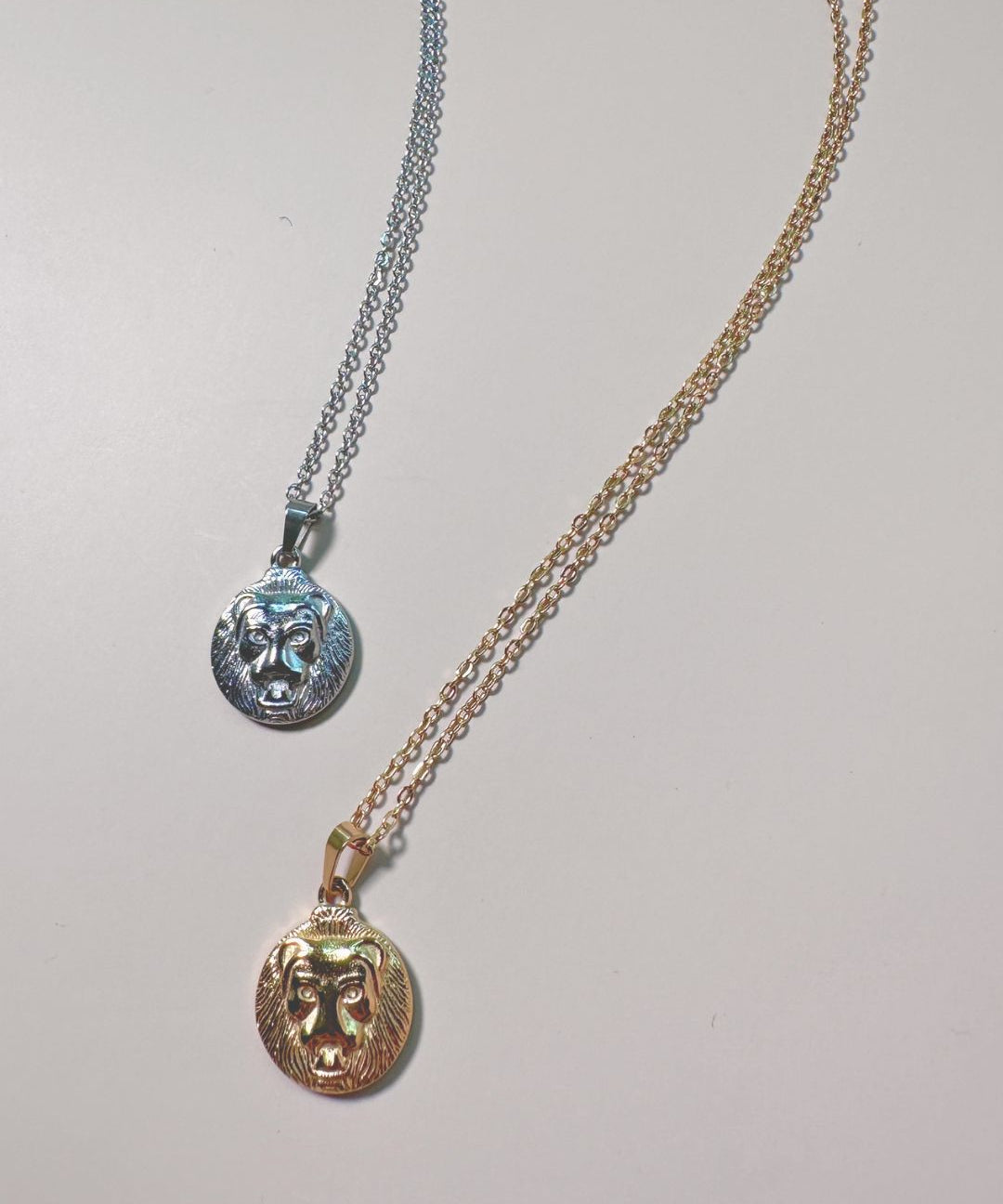 flat lay of two lion charm necklaces in gold and silver
