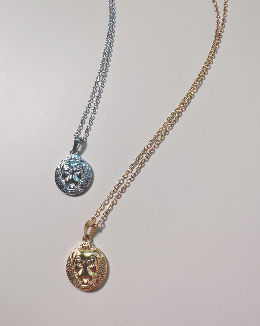 flat lay of two lion charm necklaces in gold and silver