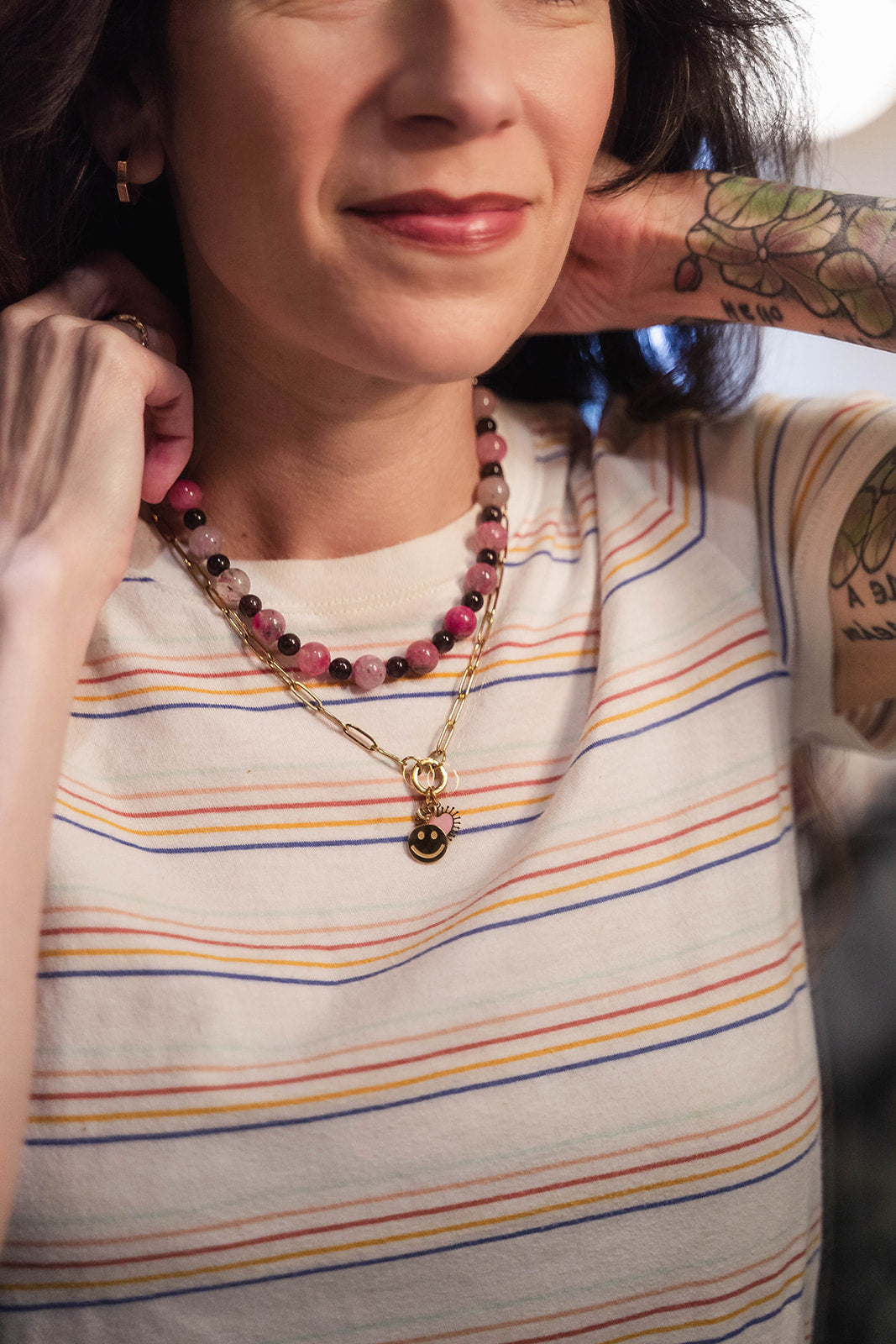 Woman wearing a striped shirt and layered necklaces with a tattooed arm.