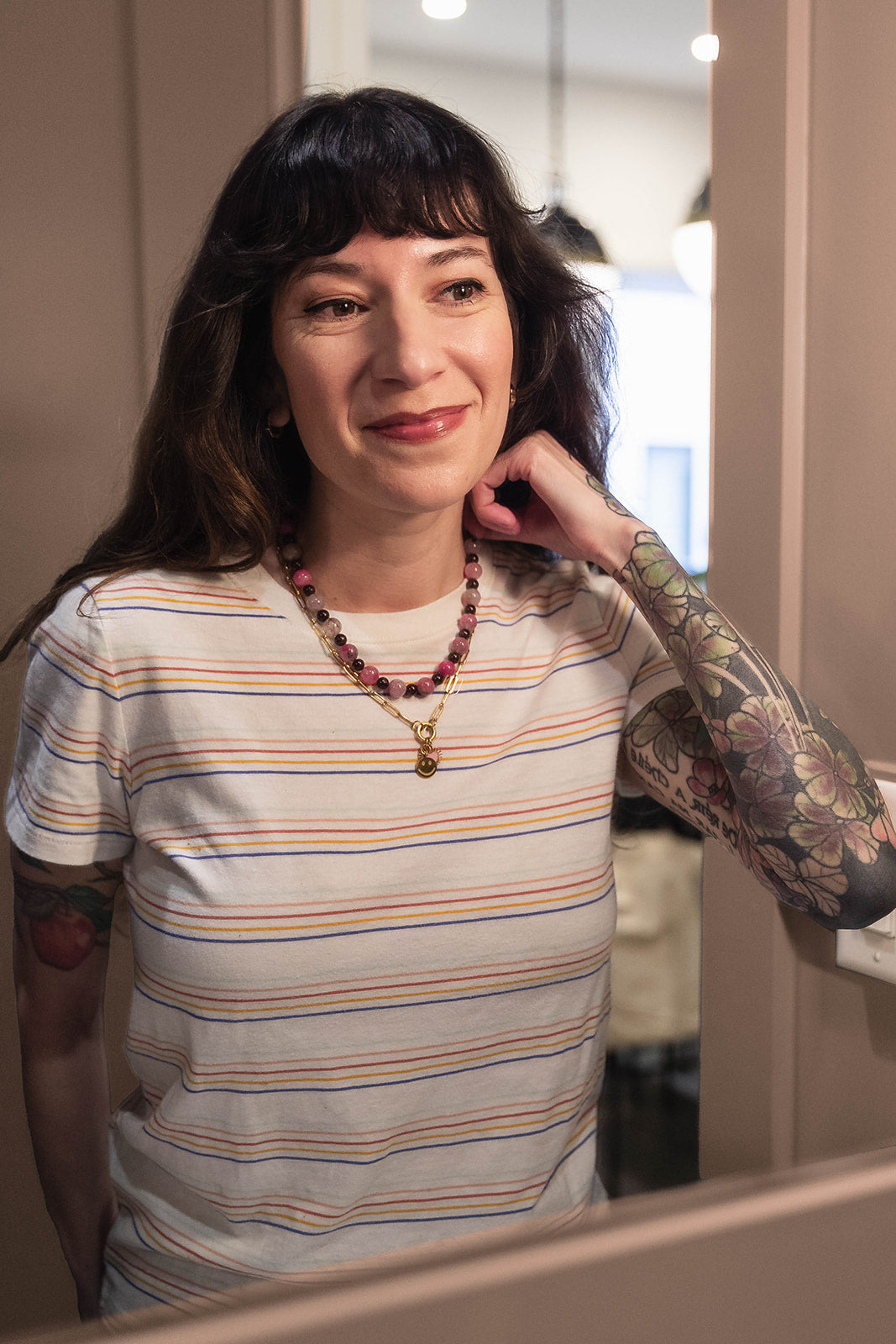 Woman with tattoos and a striped shirt standing in front of a mirror.