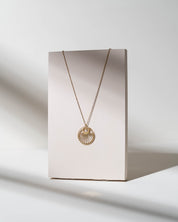 A delicate gold chain necklace with a sunburst pendant displayed on a minimalist beige card, set against a clean white background with soft shadows.