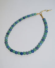 A beaded necklace made of alternating green and blue beads, finished with a gold clasp, shown on a plain light background.