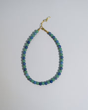 A beaded necklace made of alternating blue and green beads, finished with a gold clasp, displayed on a plain light gray background.
