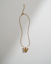 A delicate gold chain necklace featuring a small butterfly pendant, displayed against a plain white background with soft shadows.