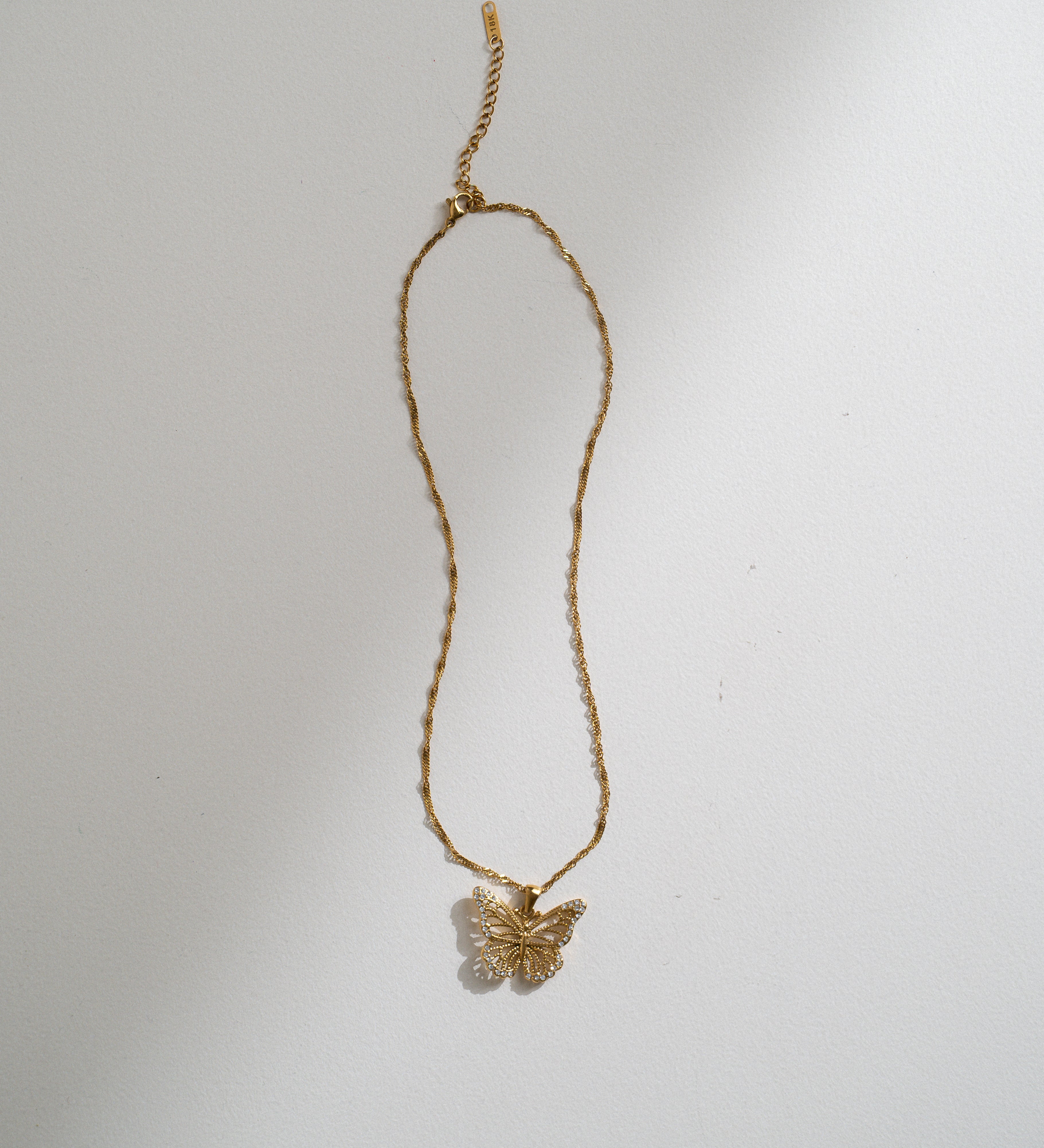 A delicate gold chain necklace featuring a small butterfly pendant, displayed against a plain white background with soft shadows.