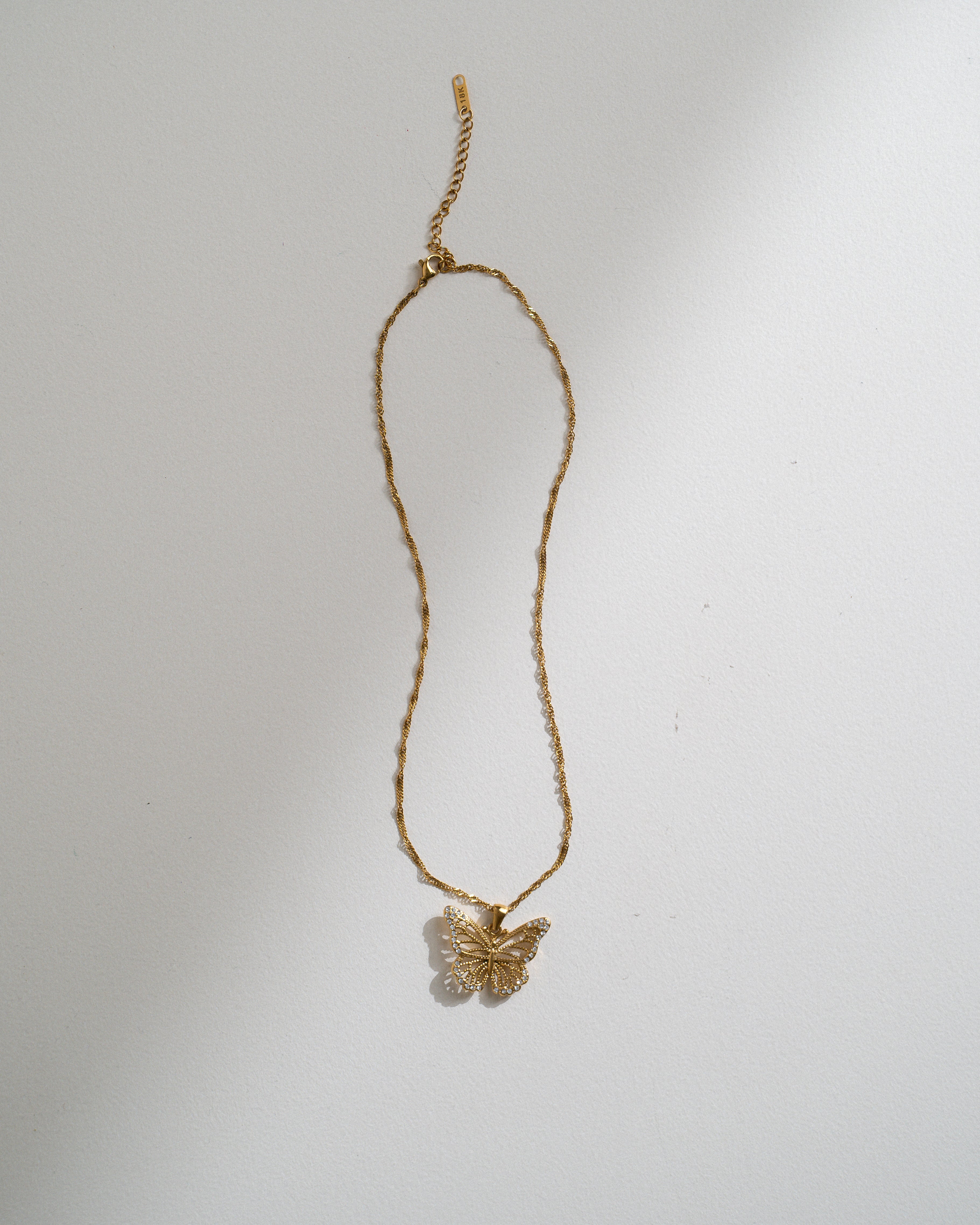 A delicate gold chain necklace featuring a small butterfly pendant, displayed against a plain white background with soft shadows.