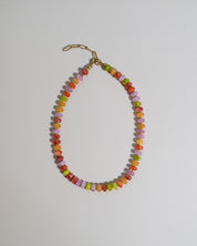 A beaded necklace made of small, faceted beads in a multicolor mix of orange, yellow, green, pink, and red, finished with a gold lobster clasp, shown on a plain light gray background.