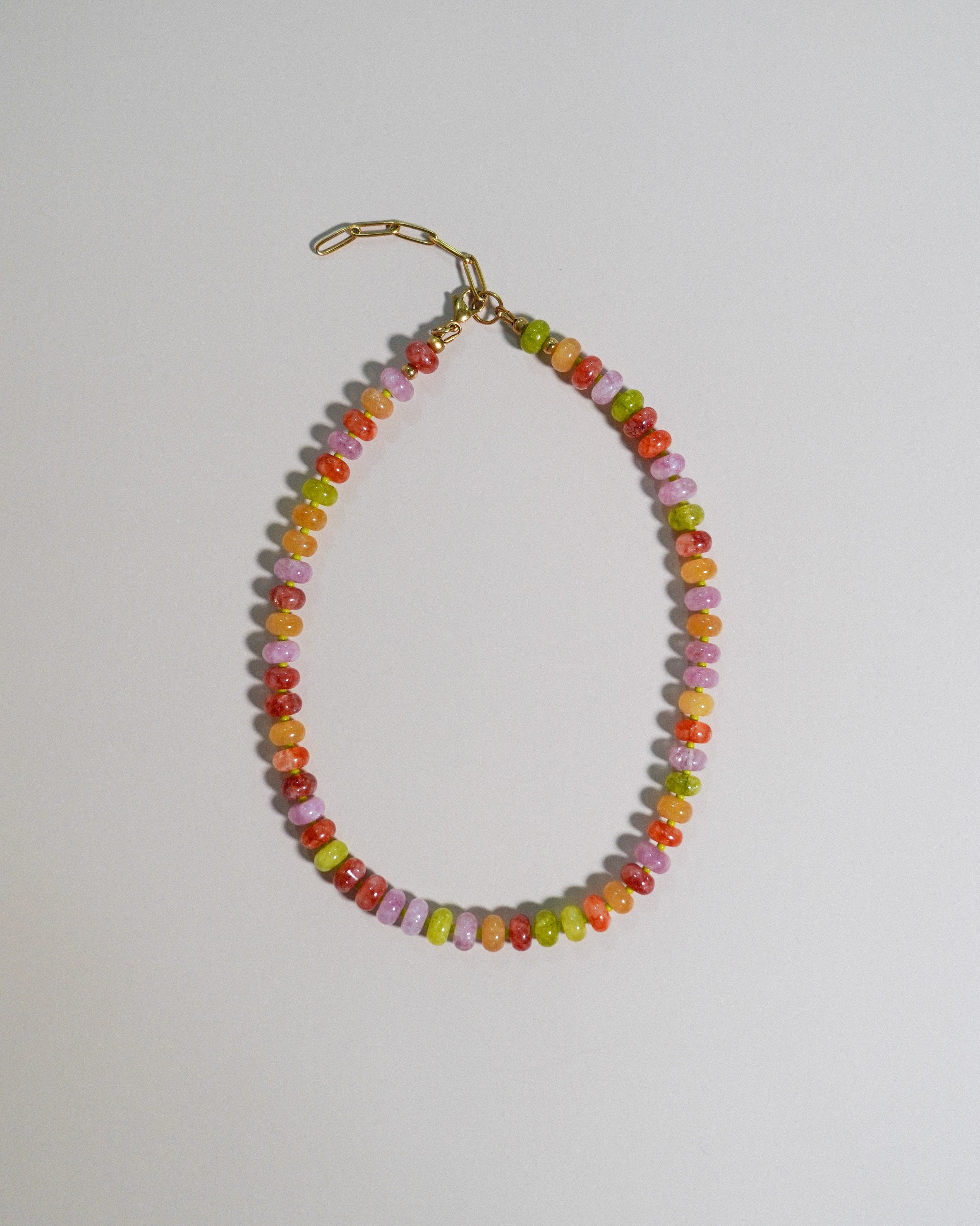 A beaded necklace made of small, faceted beads in a multicolor mix of orange, yellow, green, pink, and red, finished with a gold lobster clasp, shown on a plain light gray background.