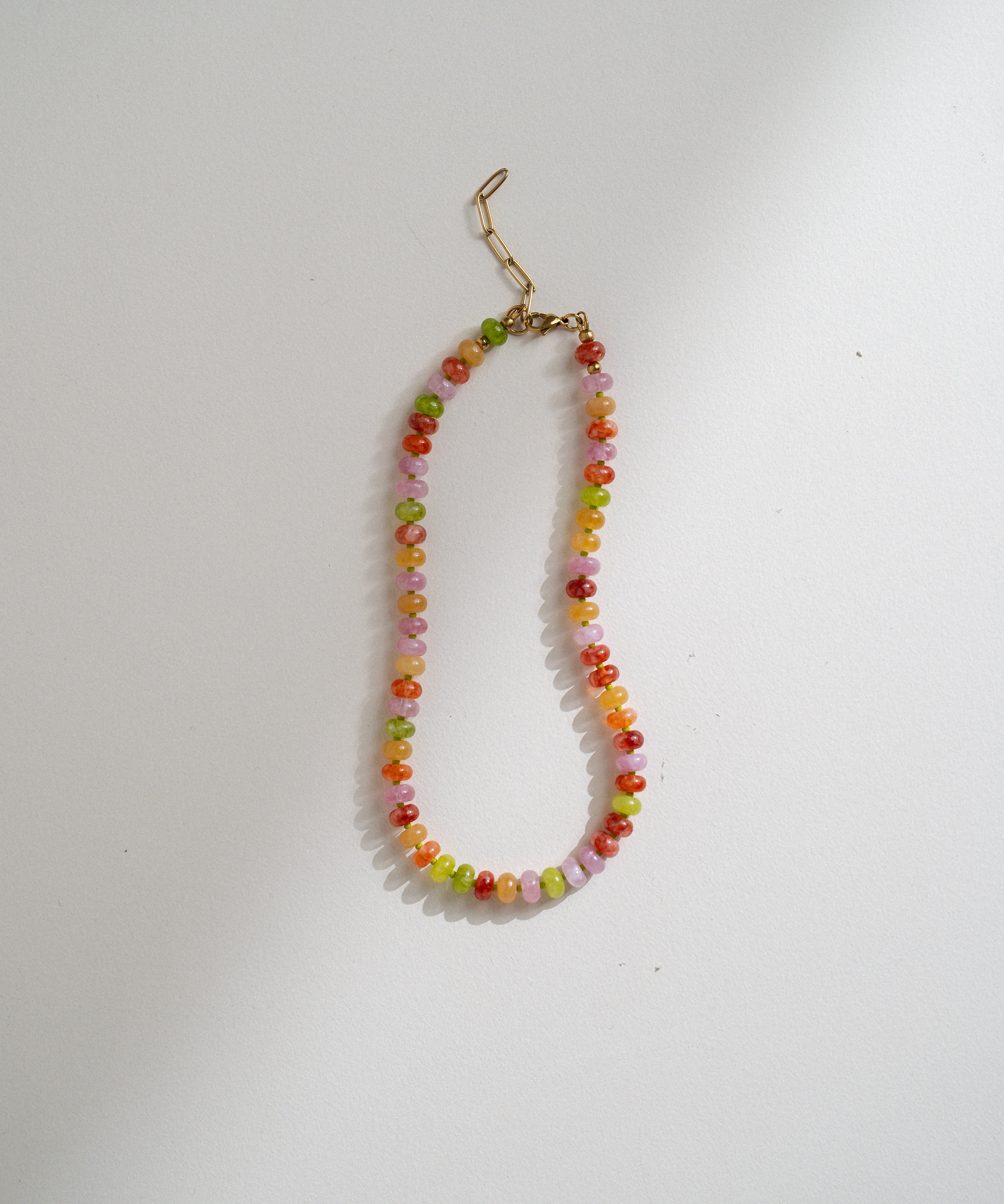 A beaded necklace with small multicolored round beads in orange, yellow, green, and pink, finished with a gold-tone lobster clasp, shown on a plain light background.