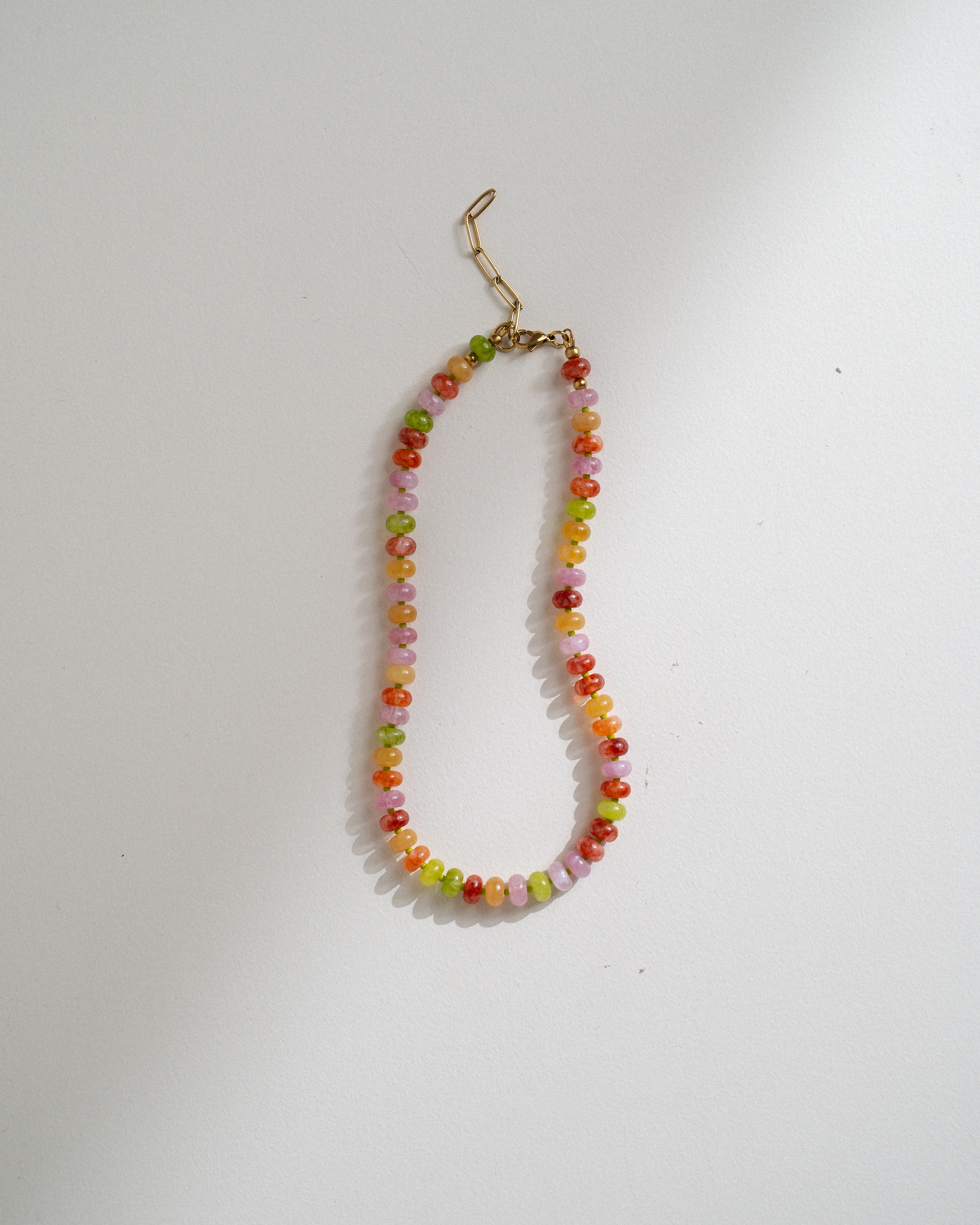 A beaded necklace with small multicolored round beads in orange, yellow, green, and pink, finished with a gold-tone lobster clasp, shown on a plain light background.