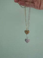 Heart-shaped pendant on a chain held by a hand against a plain background