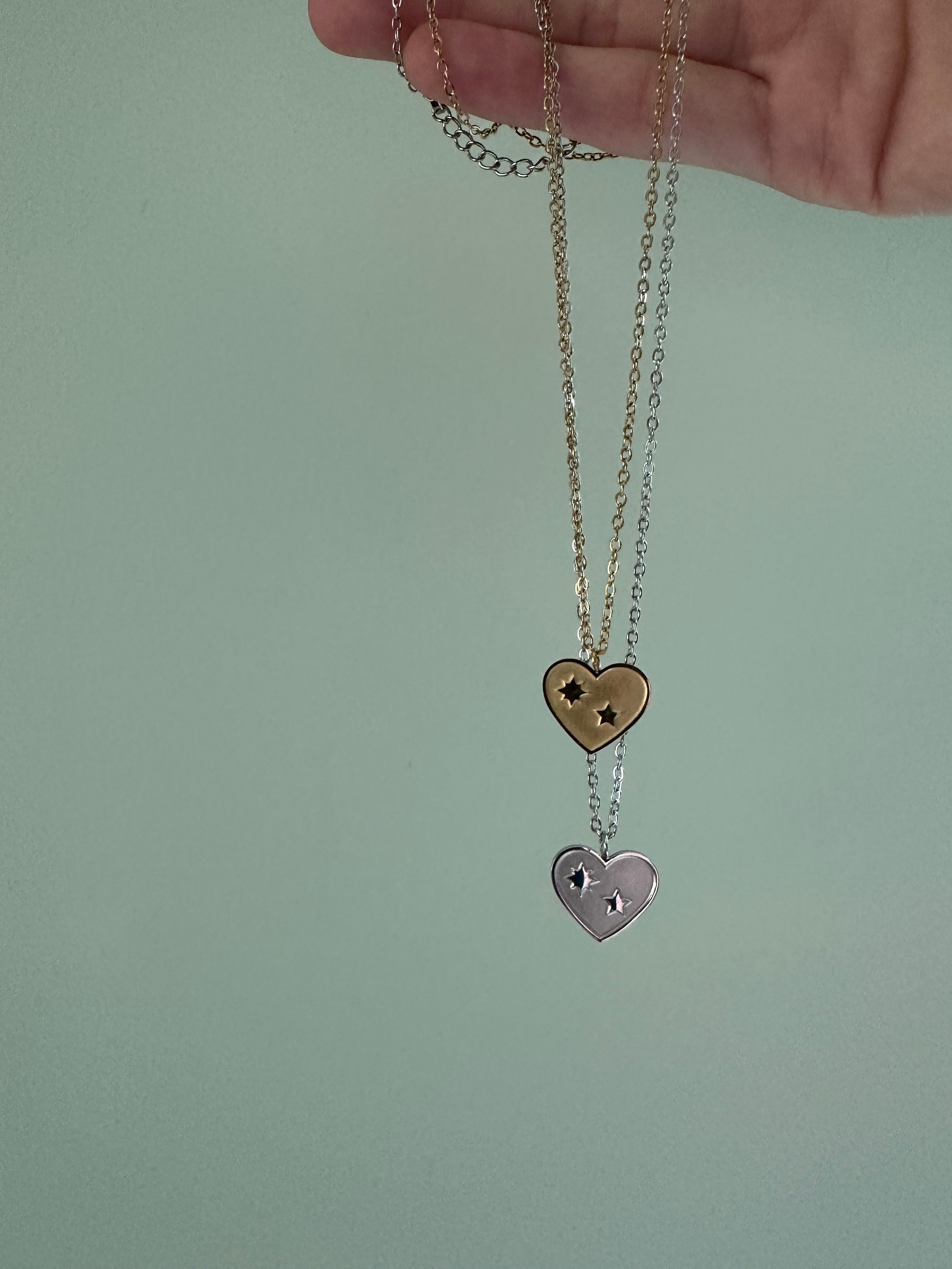 Heart-shaped pendant on a chain held by a hand against a plain background