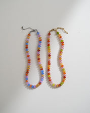 Two beaded necklaces laid flat on a white surface. One necklace has multicolored faceted beads with a silver-tone clasp and extender chain, and the other has multicolored beads with a gold-tone clasp and extender.