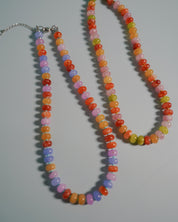 Two beaded necklaces with colorful round beads in orange, red, pink, purple, yellow, and green, displayed on a light gray background.