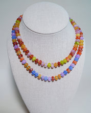 A double-strand beaded necklace displayed on a light gray fabric-covered jewelry bust. The necklace features faceted beads in multiple pastel and bright colors including orange, yellow, green, blue, purple, and red.
