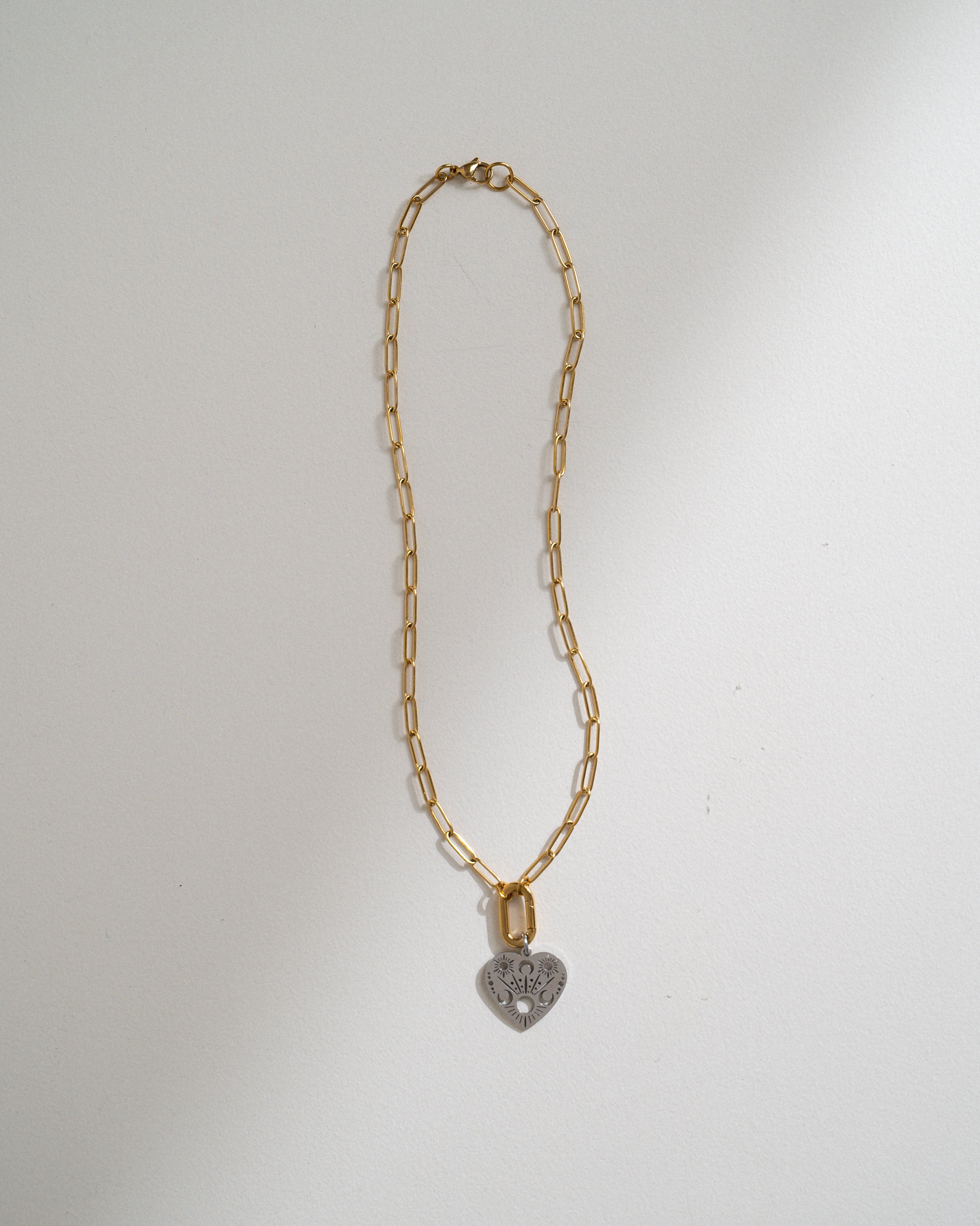 A gold paperclip chain necklace with a small heart-shaped pendant, photographed against a plain white background.