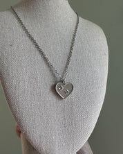 Silver necklace with a heart-shaped pendant on a mannequin bust against a gray background
