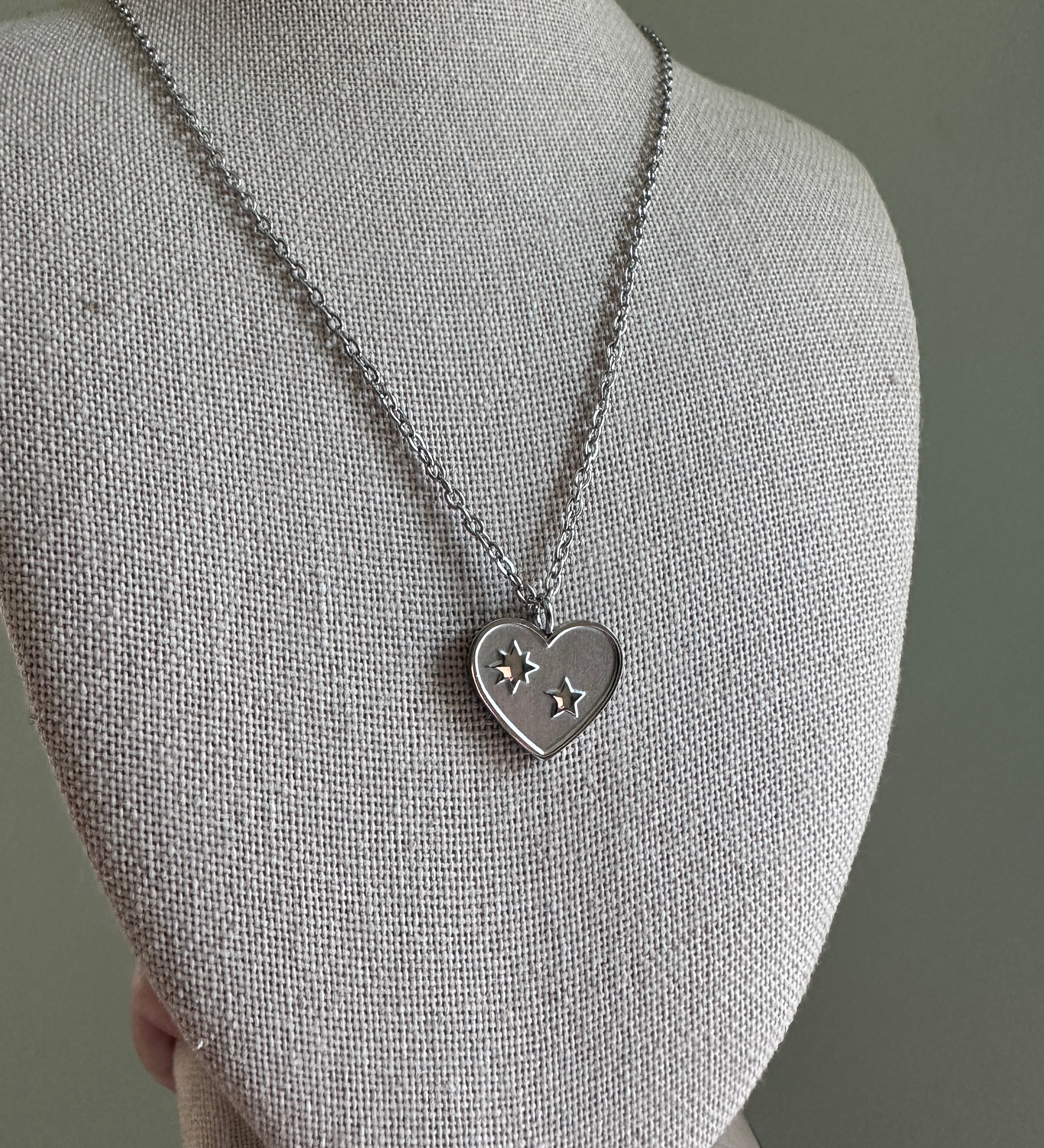 Silver necklace with a heart-shaped pendant on a mannequin bust against a gray background