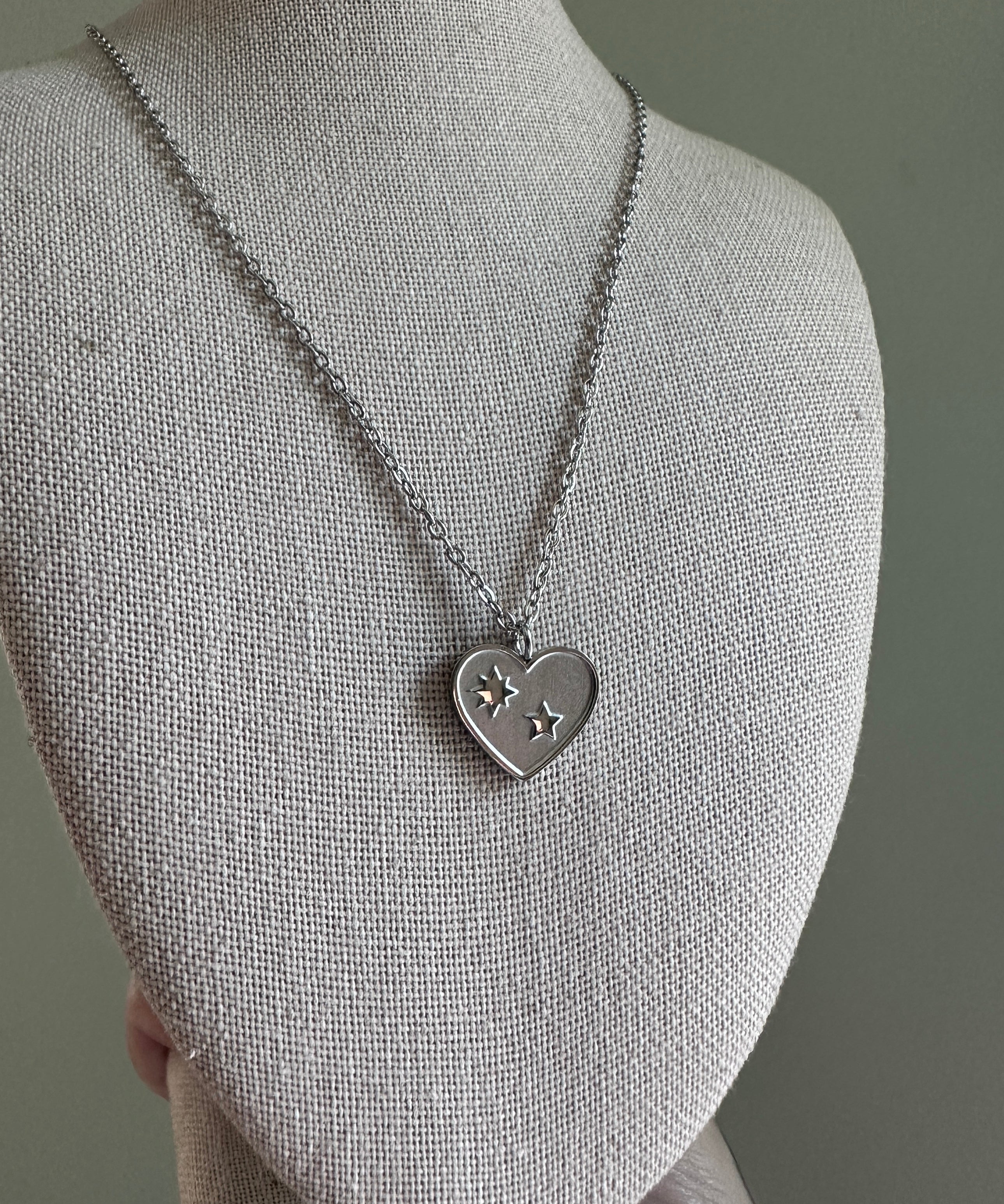 Silver necklace with a heart-shaped pendant on a mannequin bust against a gray background