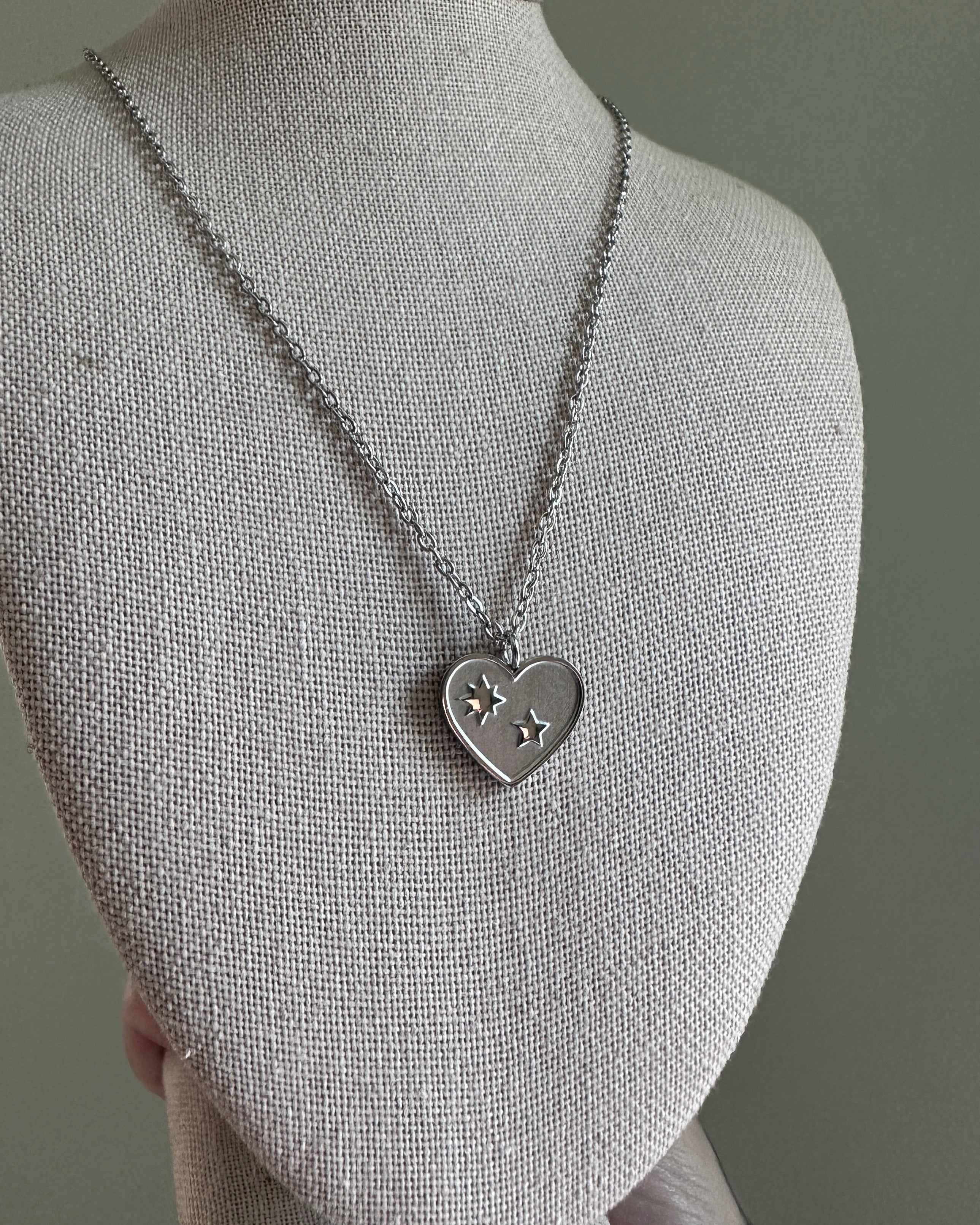 Silver necklace with a heart-shaped pendant on a mannequin bust against a gray background
