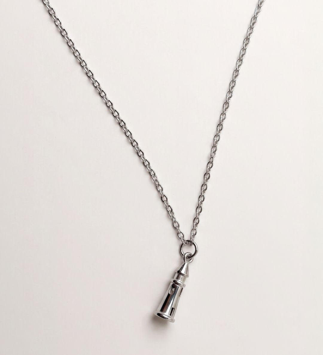A silver-toned chain necklace with a small lighthouse charm, shown on a plain light background.