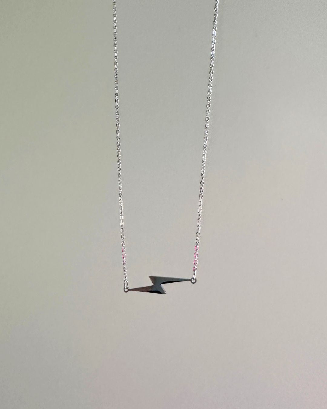 silver lightning bolt necklace hanging in front of gray wall